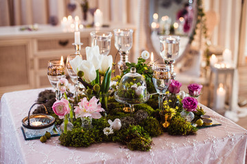 A table for two. Romantic atmosphere in subdued light, lighted candles and rustic decoration (forest moss, flowers, glasses and vases)