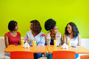 Four young african girls with juices sitting in bright colored fast food restaurant.