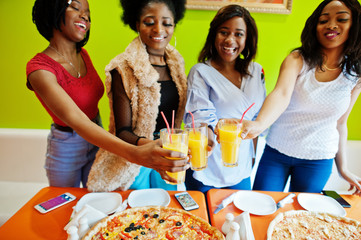 Four young african girls in bright colored pizza restaurant clinking juices.