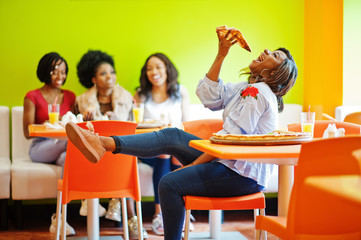 African woman with pizza sitting at restaurant against dark skinned girls.
