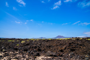 Spain, Lanzarote, Majestic volcano monte corona behind endless field of lava and green vegetation