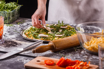 young woman in a gray aprong prepares a vegetarian pizza