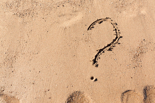 Question mark sign on sand beach near the sea. Concept of dilemma, answer and question