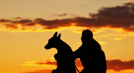 Silhouettes of girl and dog at sunset, breed Belgian shepherd Malinois, incredibly beautiful sunset, best friends together