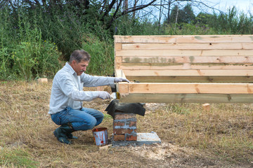 Fototapeta premium Construction of a wooden house in a rural area. A grown man is painting the house.