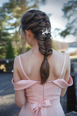 Elegant hairstyle is not a young girl in a pink dress on the nature, rear view.