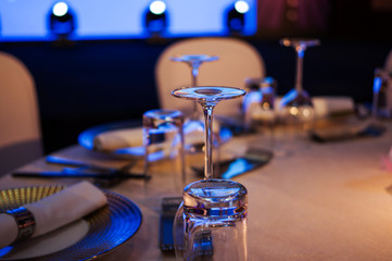 Upside down wine glasses, plates, napkin and chopsticks on dinner table with blue stage light