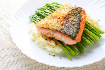 Grilled salmon garnished with asparagus and herbs and mashed potatoes, served on white plated..