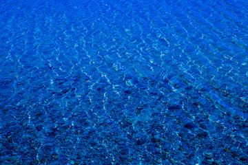 Blue water surface with ripples through which the sandy bottom with pebbles is visible