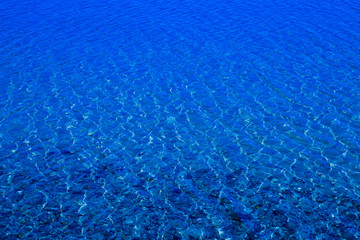 Blue water surface with ripples through which the sandy bottom with pebbles is visible