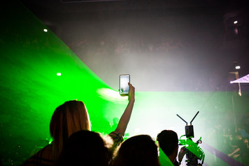 woman taking pictures at an event with a smartphone against green neon lights