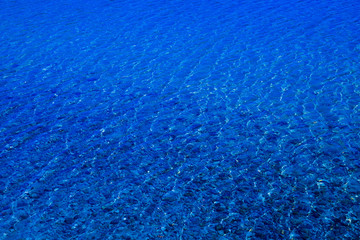 Blue water surface with ripples through which the sandy bottom with pebbles is visible