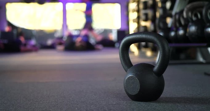 A kettlebell weight in a gym with people working out in a fitness training class in the background SLIDE RIGHT.