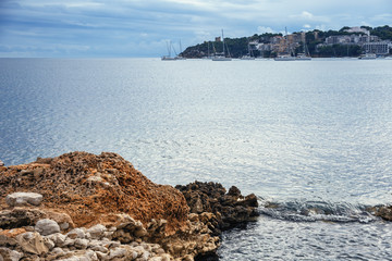 view of a quiet harbor with yachts in the Spanish city of Magaluf with a textured rock and a wave...