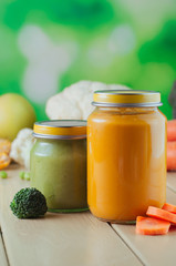 Carrot and broccoli puree in glass jars on wooden background