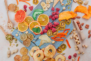 Dried fruit and vegetable chips, candied pumpkin slices, nuts and seeds on blue wooden board