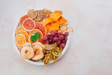 Mixed dried fruit and vegetable chips in round ceramic plate on beige concrete background
