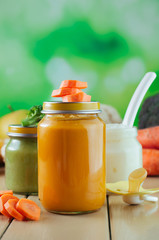 Jars with vegetable puree near fresh broccoli, cauliflower and carrot