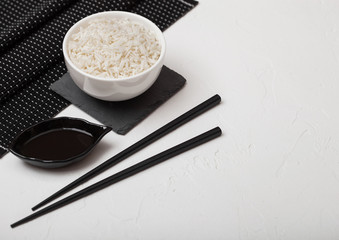 White bowl with boiled organic basmati jasmine rice with black chopsticks and sweet soy sauce on bamboo place mat on white background. Space for text