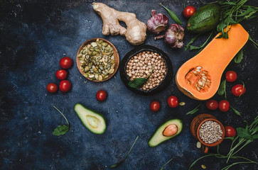 ingredients for vegetarian salad with pumpkin, tomatoes, avocado, ginger root, garlic, pumpkin and sunflower seeds, arugula salad on blue background, top view, copy space