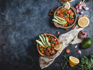 vegetarian salad with roasted pumpkin, chickpea, tomatoes, pumpkin and sunflower seeds, avocado, lemon and spices in bowls on blue background, copy space
