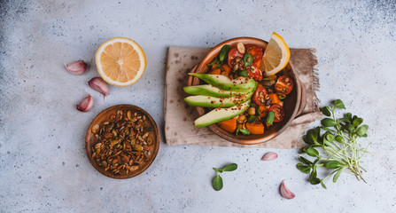 healthy vegetarian salad with roasted pumpkin, chickpea, tomatoes, pumpkin and sunflower seeds, garlic and green herbs, avocado and spices on gray background, top view, copy space