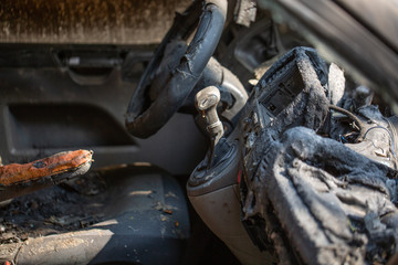 inside view of burnt out wreckage of a stolen car. Crime scene image of vehicle interior ruined by fire or arson. molten plastic and metal and steering wheel.