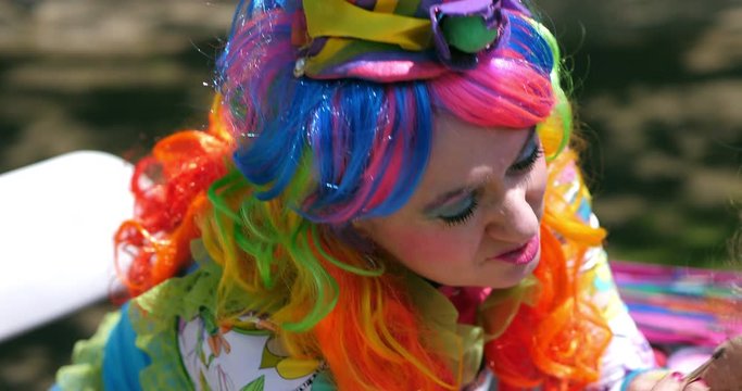 Multi-colored makeup artist clown performing face painting with kids during birthday party, 4K