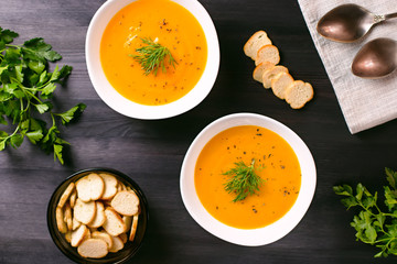 Pumpkin cream soup with croutons and fresh dill and parsley on dark wooden background, top view