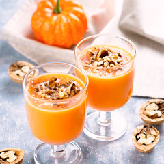 Healthy pumpkin smoothie with walnuts and cinnamon in glasses on rustic background