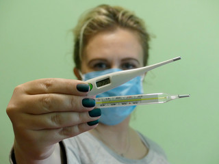 The girl in a medical mask shows thermometers. Several thermometers in the hands of the girl,...