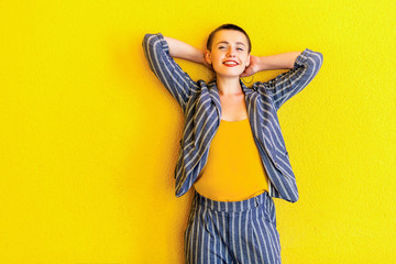 Fototapeta premium Portrait of happy young short hair beautiful woman in yellow shirt and striped suit standing, holding her head and looking at camera with toothy smile. indoor studio shot isolated on yellow background