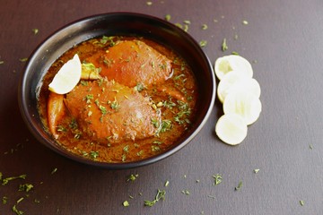 Indian Cuisine, Spicy Crabs Curry in red gravy, garnished with fresh coriander and lemon wedges or lemon slices on dark moody background