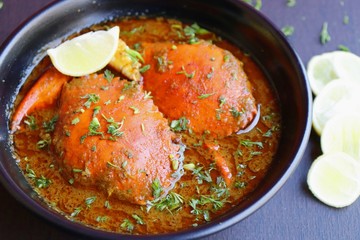 Indian Cuisine, Spicy Crabs Curry in red gravy, garnished with fresh coriander and lemon wedges or lemon slices on dark moody background