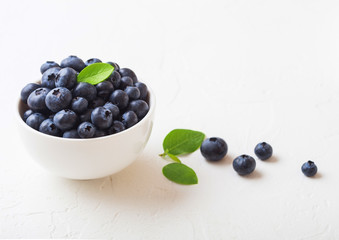 Fresh raw organic blueberries with leaf in white china bowl on white background. Macro close up