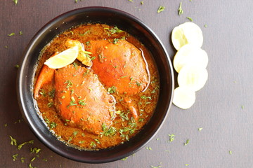 Indian Cuisine, Spicy Crabs Curry in red gravy, garnished with fresh coriander and lemon wedges or lemon slices on dark moody background