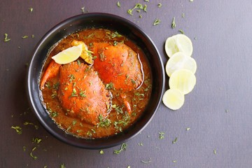 Indian Cuisine, Spicy Crabs Curry in red gravy, garnished with fresh coriander and lemon wedges or lemon slices on dark moody background