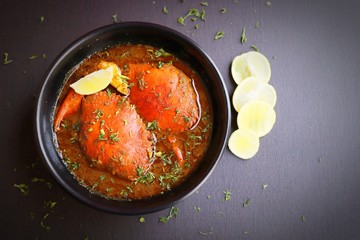 Indian Cuisine, Spicy Crabs Curry in red gravy, garnished with fresh coriander and lemon wedges or lemon slices on dark moody background