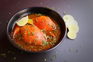Indian Cuisine, Spicy Crabs Curry in red gravy, garnished with fresh coriander and lemon wedges or lemon slices on dark moody background