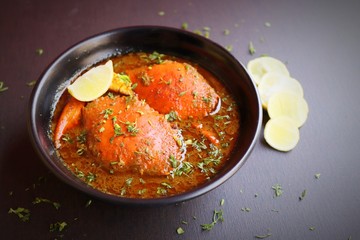 Indian Cuisine, Spicy Crabs Curry in red gravy, garnished with fresh coriander and lemon wedges or lemon slices on dark moody background