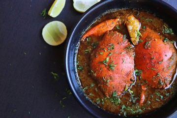 Indian Cuisine, Spicy Crabs Curry in red gravy, garnished with fresh coriander and lemon wedges or lemon slices on dark moody background