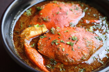 Indian Cuisine, Spicy Crabs Curry in red gravy, garnished with fresh coriander and lemon wedges or lemon slices on dark moody background