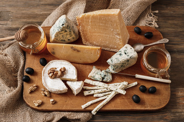 Different types of cheeses. slices of cheese brie or camembert with parmesan, cheddar ,blue cheese , and other with nut and honey on wooden board on dark background