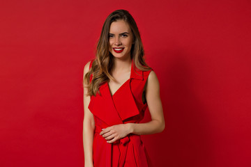 Smiling lovely woman with long hair and evening make up posing over red background and looking at camera