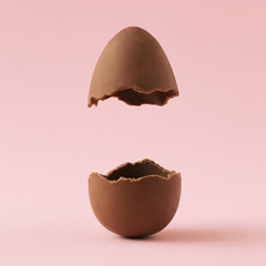 Chocolate Easter egg broken in half on pastel pink background with creative copy space. Minimal...