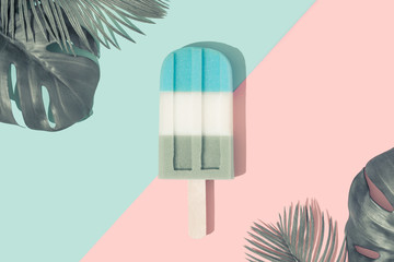 Ice cream popsicle in pastel blue on paper duotone background with tropical palm leaves. Minimal summer concept. Flat lay.