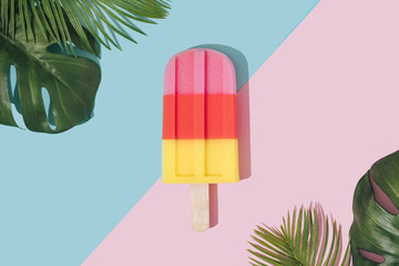 Ice cream popsicle in pastel pink on paper duotone background with tropical palm leaves. Minimal...