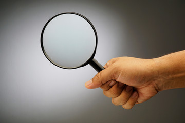 Man's hand, holding classic styled magnifying glass, close-up isolated on grey background, copy space for your image or text.