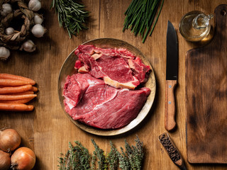 Fresh chunks of red meat on vintage plate with different vegetables on wooden table