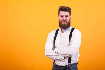 Portrait of young bearded man with arms crossed looking at the camera over yellow background